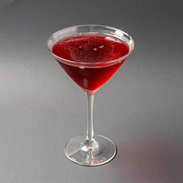 A vibrant red cocktail in a martini glass, with a frothy top, against a dark background.