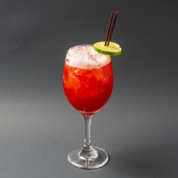 Red Italian cocktail with foam, lime slice, and two brown straws in a wine glass.