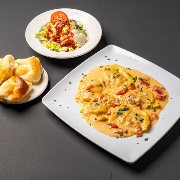 Bella's Italian Restaurant's ravioli in creamy sauce with tomatoes, a side salad, and garlic knots.