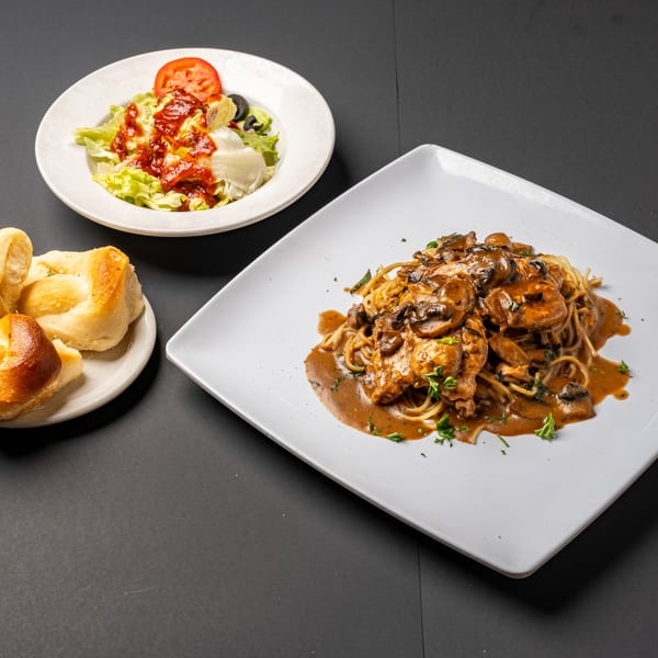 Bella's Italian Restaurant's chicken marsala with spaghetti, a side salad, and bread rolls.