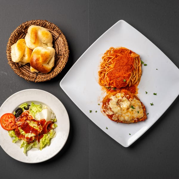 Bella's Italian Restaurant's spaghetti, chicken parmesan, side salad, and bread rolls on a dark background.