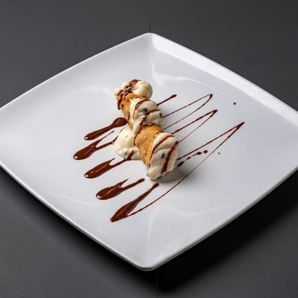 Two cannoli filled with cream and chocolate chips, drizzled with chocolate sauce on a white plate.