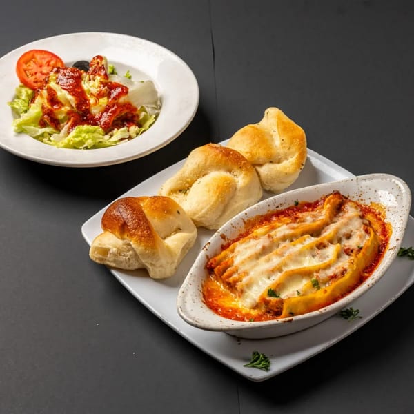 Baked manicotti with melted cheese, garlic knots, and a side salad with tomato and olives.